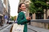 Girl in green suit jacket smiling as she holds her phone walking outside