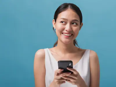 Girl holding mobile phone as she smiles looking off to the side