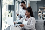 Man and woman sitting on and around couch looking at laptop and smiling