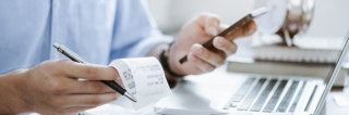 Person sitting at desk looking at their phone and holding a receipt