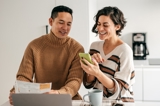 Couple standing at a table looking at their phone and laptop together