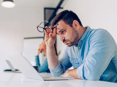 Man sitting at desk in front of his laptop looking exhausted