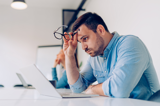 Man sitting at desk in front of his laptop looking exhausted