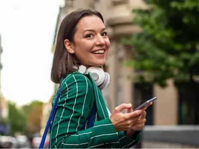 Girl in green suit jacket smiling as she holds her phone walking outside