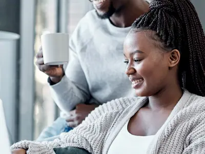 Man and woman sit on and around couch looking at their laptop together 