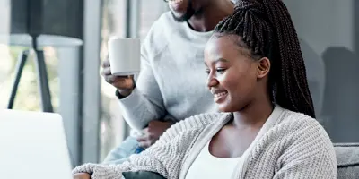 Man and woman sit on and around couch looking at their laptop together